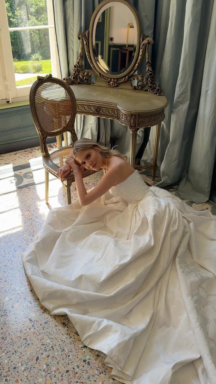 Bride in a white gown sitting on the floor beside a vintage chair