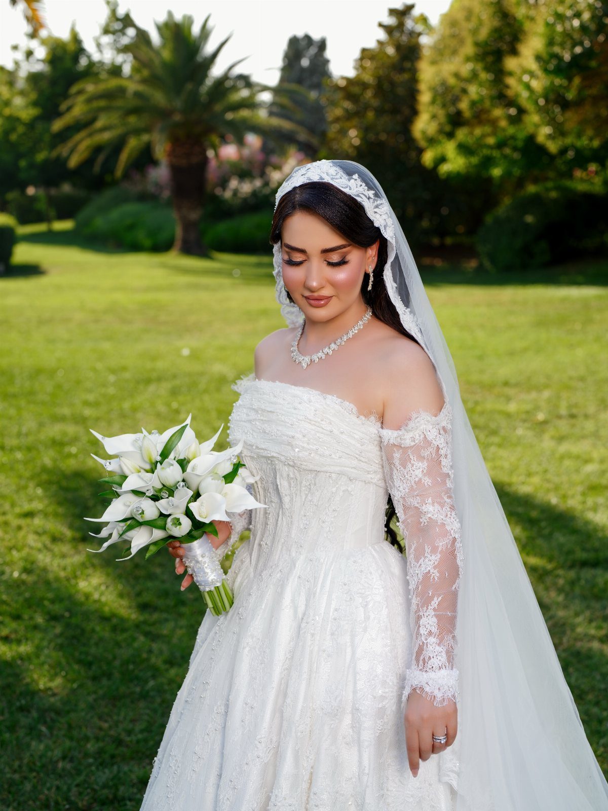 Bride in white lace dress looking down at her white calla lily bouquet.
