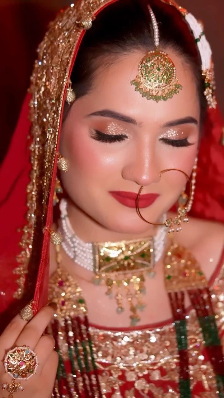 Bride in red and gold traditional attire wearing ornate jewelry with eyes closed.