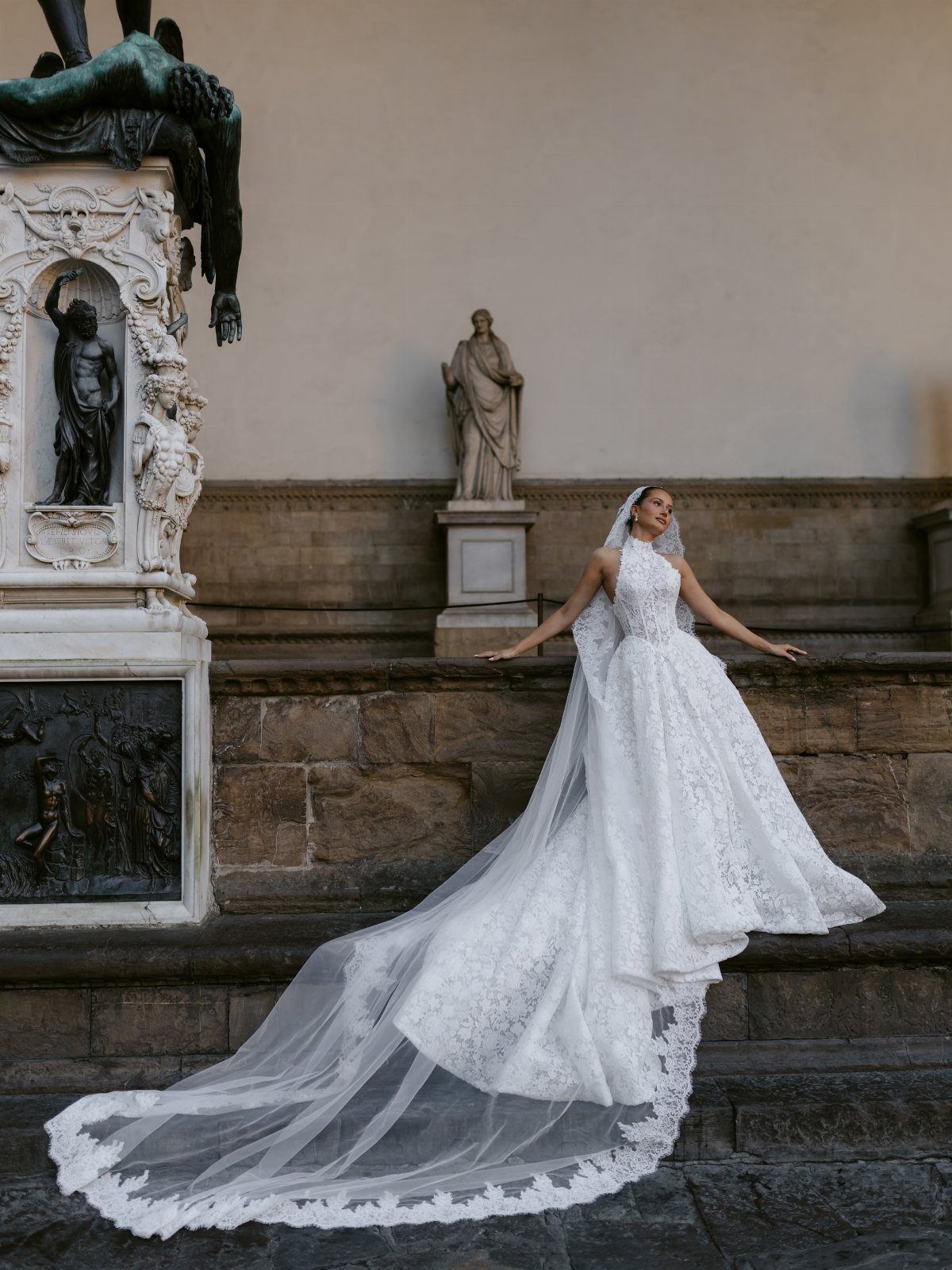 Bride in a white lace wedding dress posing on stone stairs by sculptures