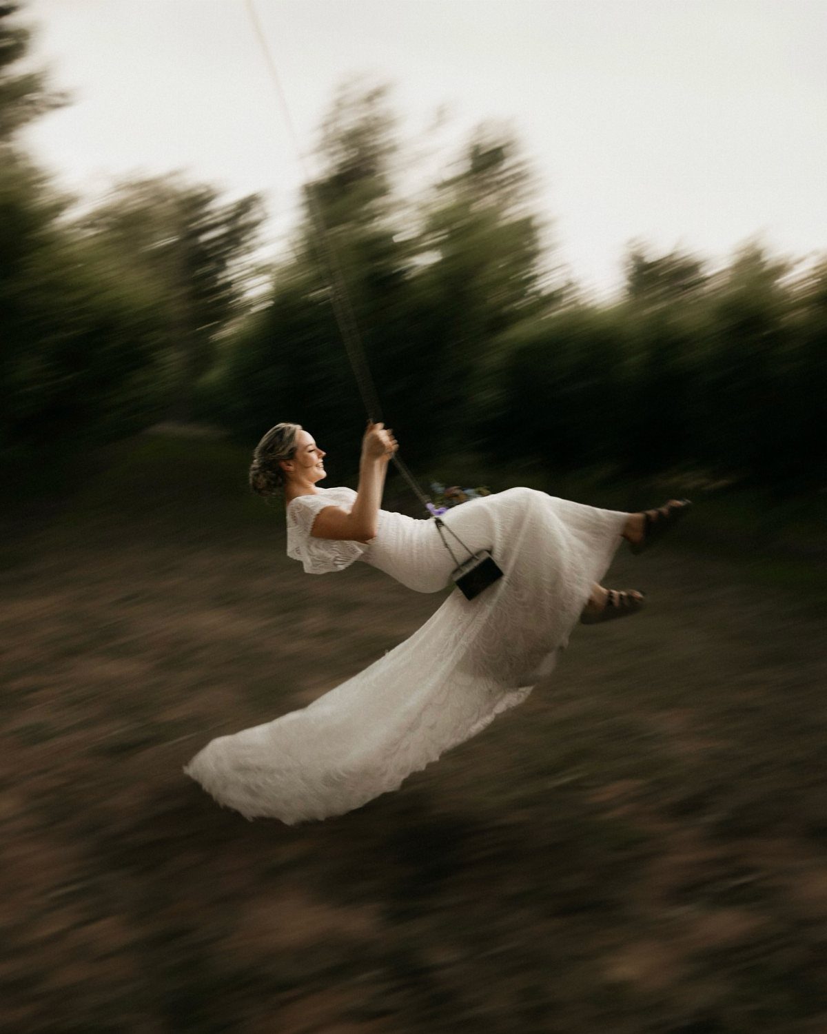 Bride in a white wedding dress swinging through a blurred forest landscape