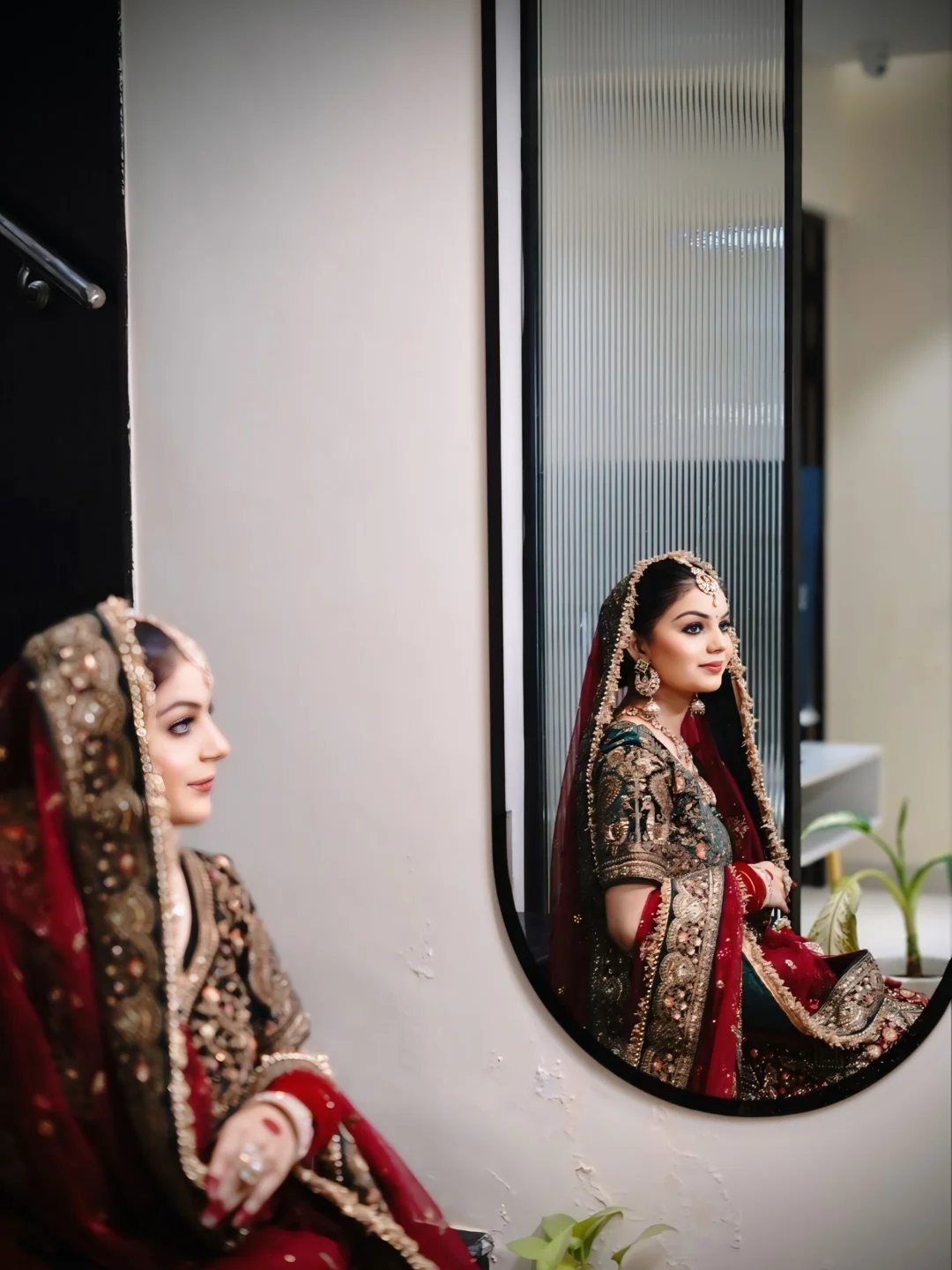 Bride in red embroidered wedding attire looking at her reflection in an oval mirror.
