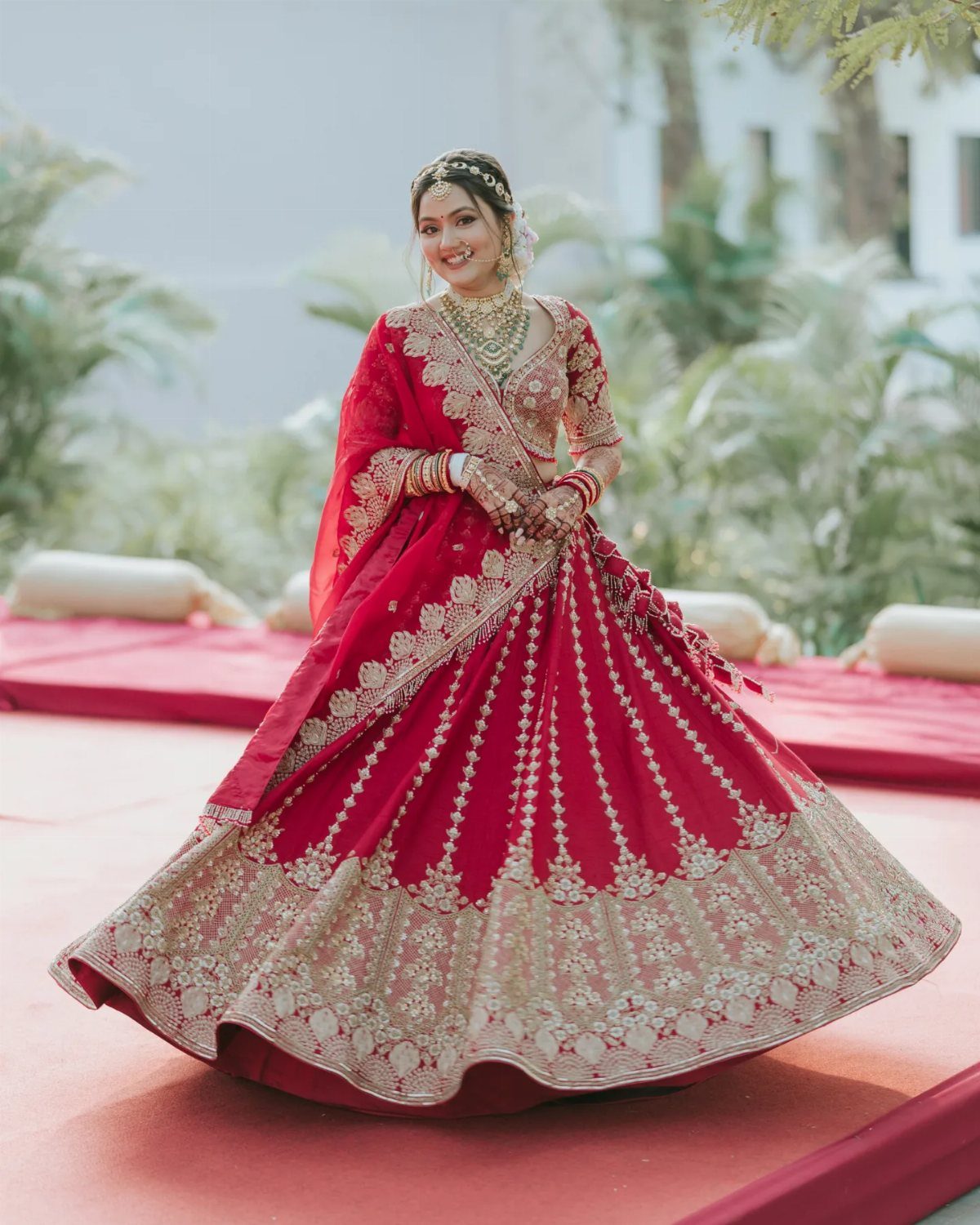 Bride in red lehenga twirling, showcasing the movement of her embroidered wedding dress.