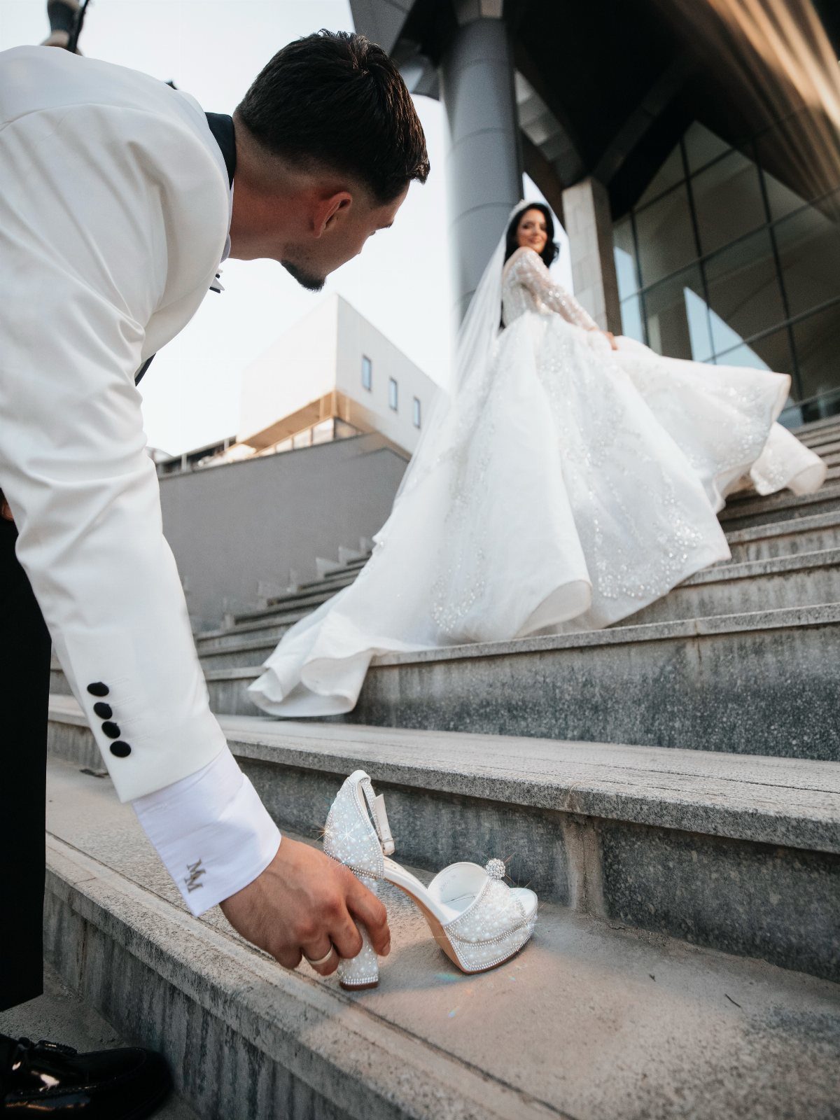 Groom picking up a bridal shoe on stairs with bride in background