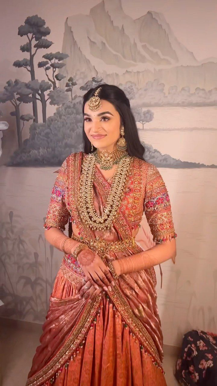Woman in red and gold lehenga posing with hands clasped in front.