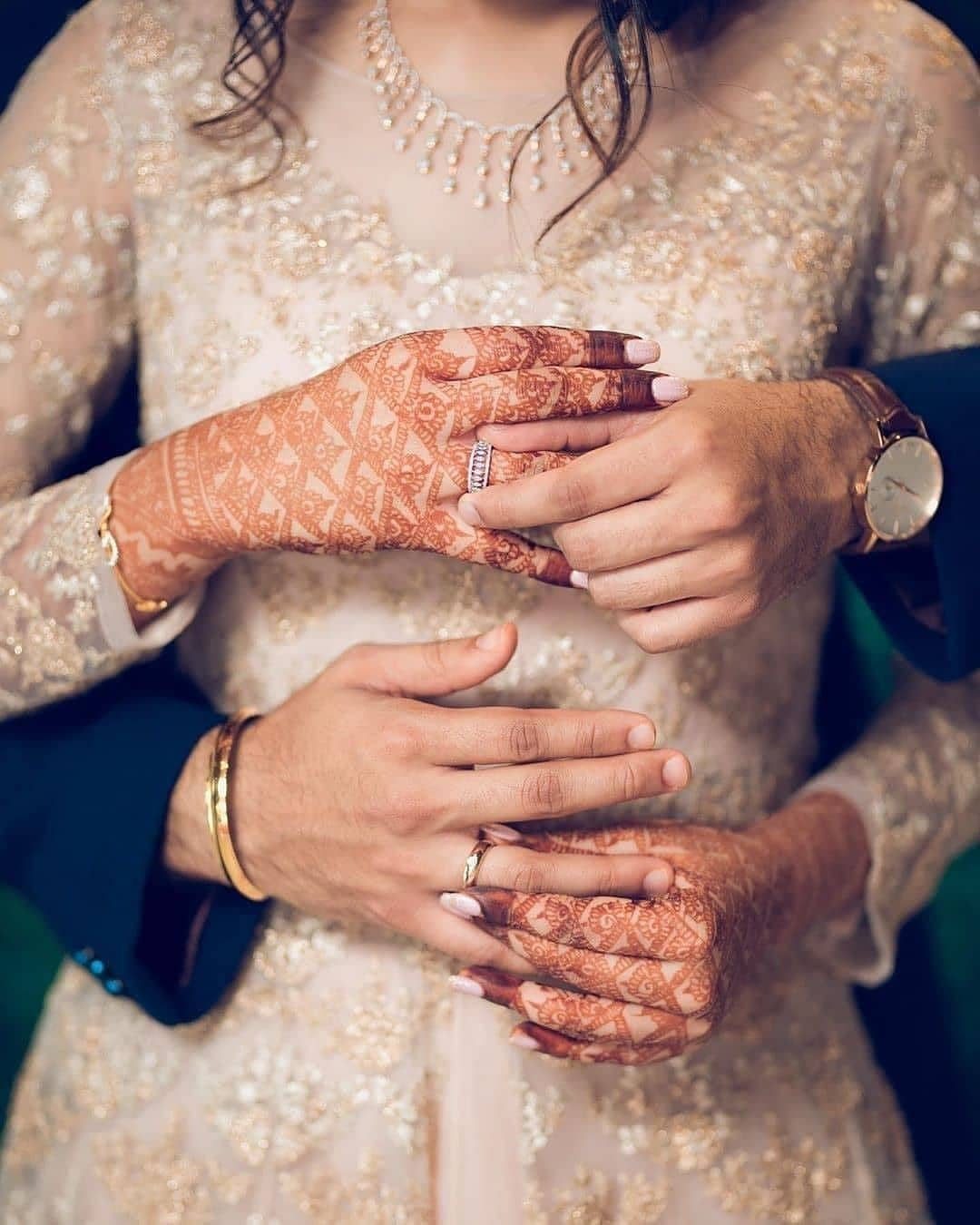 Bride and groom's hands with henna and wedding rings on embroidered dress