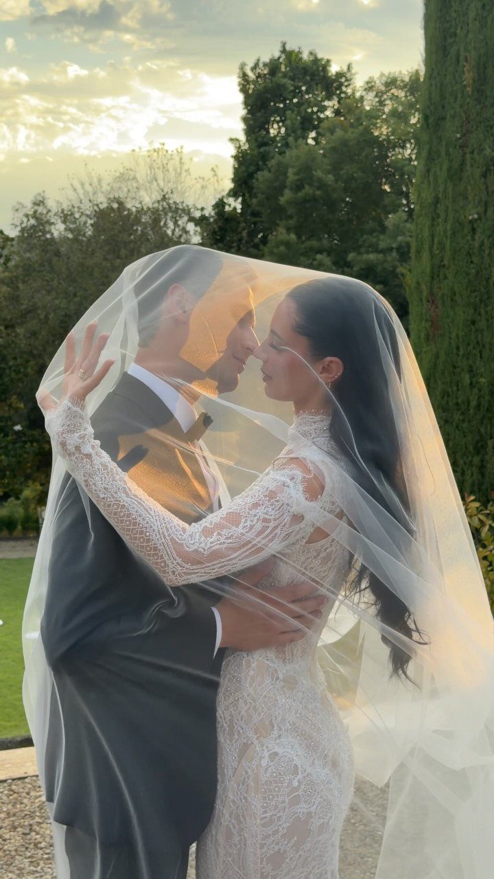Bride and groom embracing under a sheer white veil during a sunset outdoor shoot.