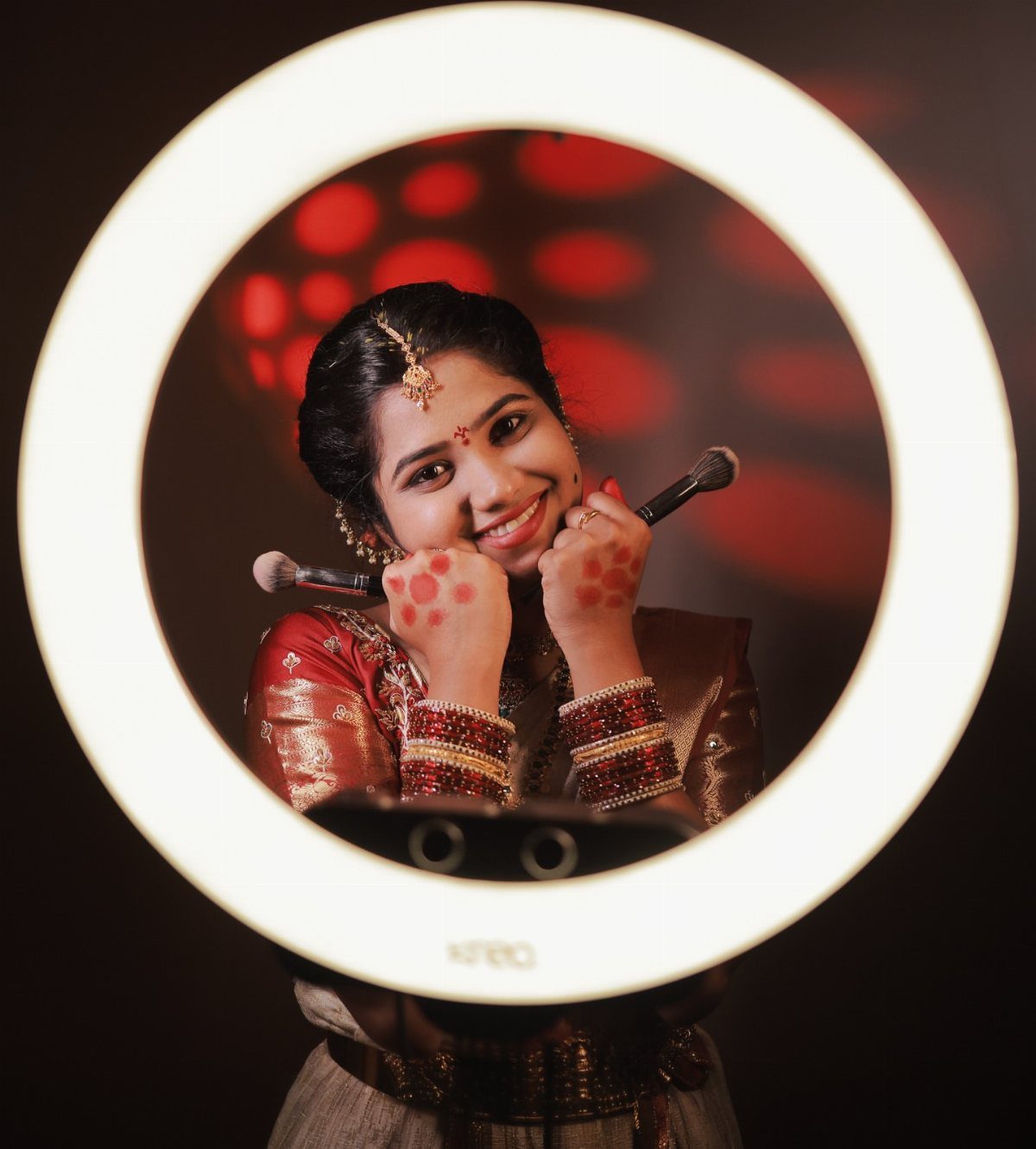 Smiling bride in traditional red attire framed by a bright circular ring light