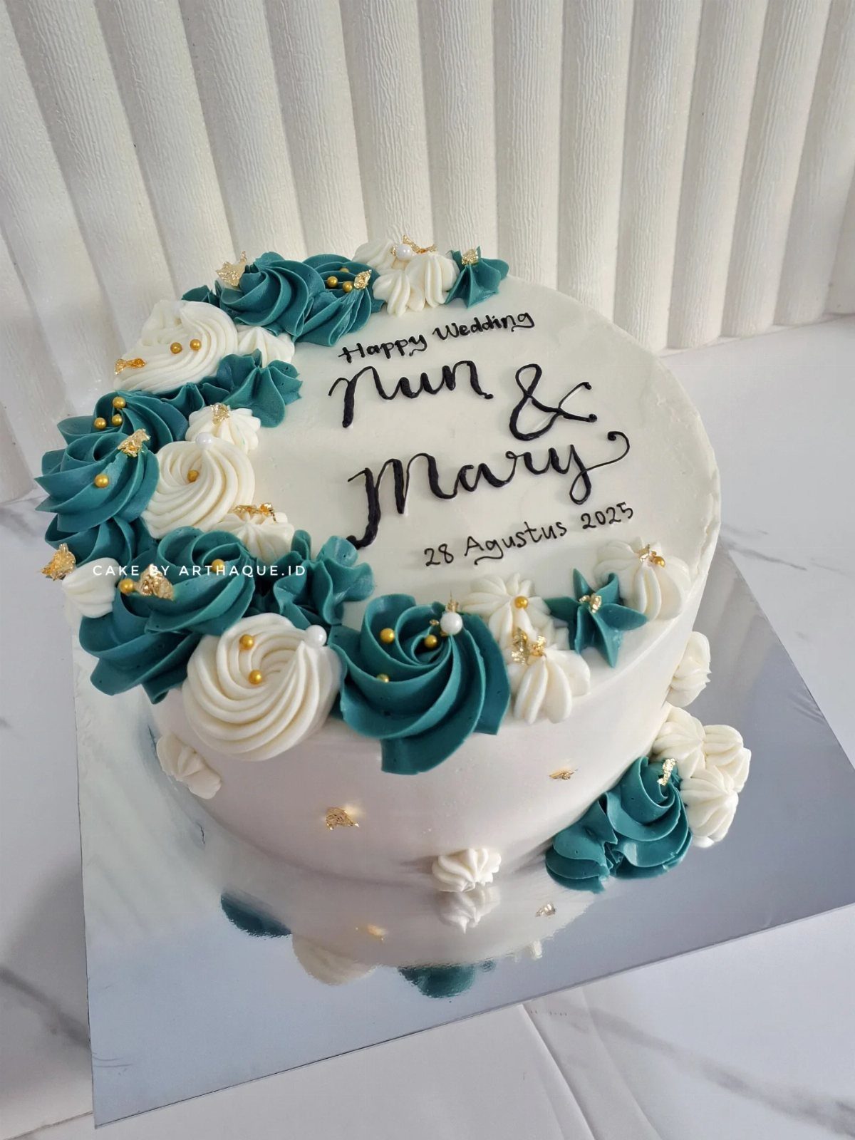 White buttercream wedding cake with teal swirls and gold pearls on silver board
