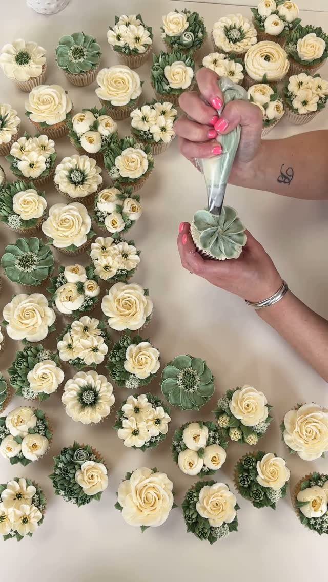 Hands piping green buttercream frosting onto a cupcake among many floral cupcakes.