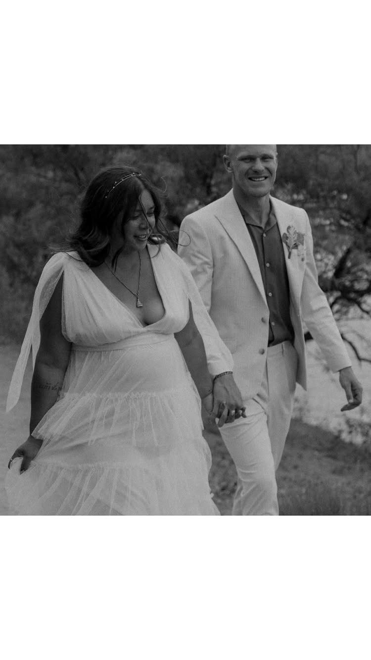 Bride and groom walking hand-in-hand and smiling in a black and white outdoor shot.