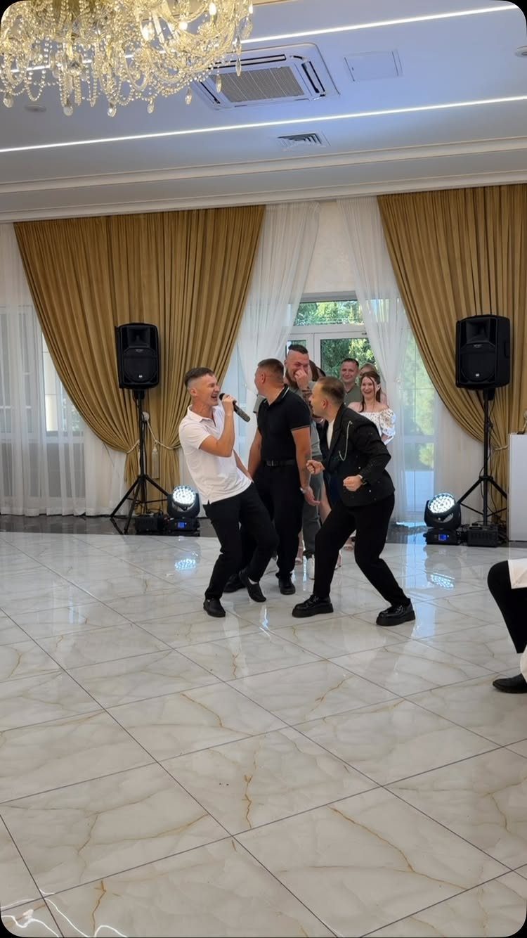 Men dancing and singing on a marble floor in a decorated banquet hall.