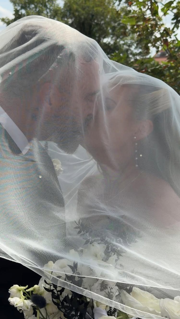 Bride and groom kissing under a white veil with a floral bouquet
