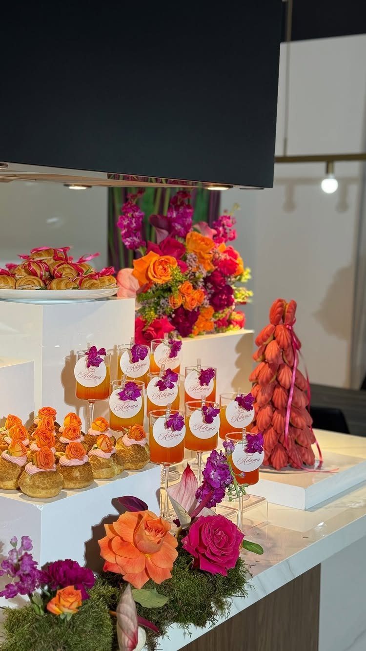 Catered appetizers and orange drinks displayed with colorful roses on white tiers.