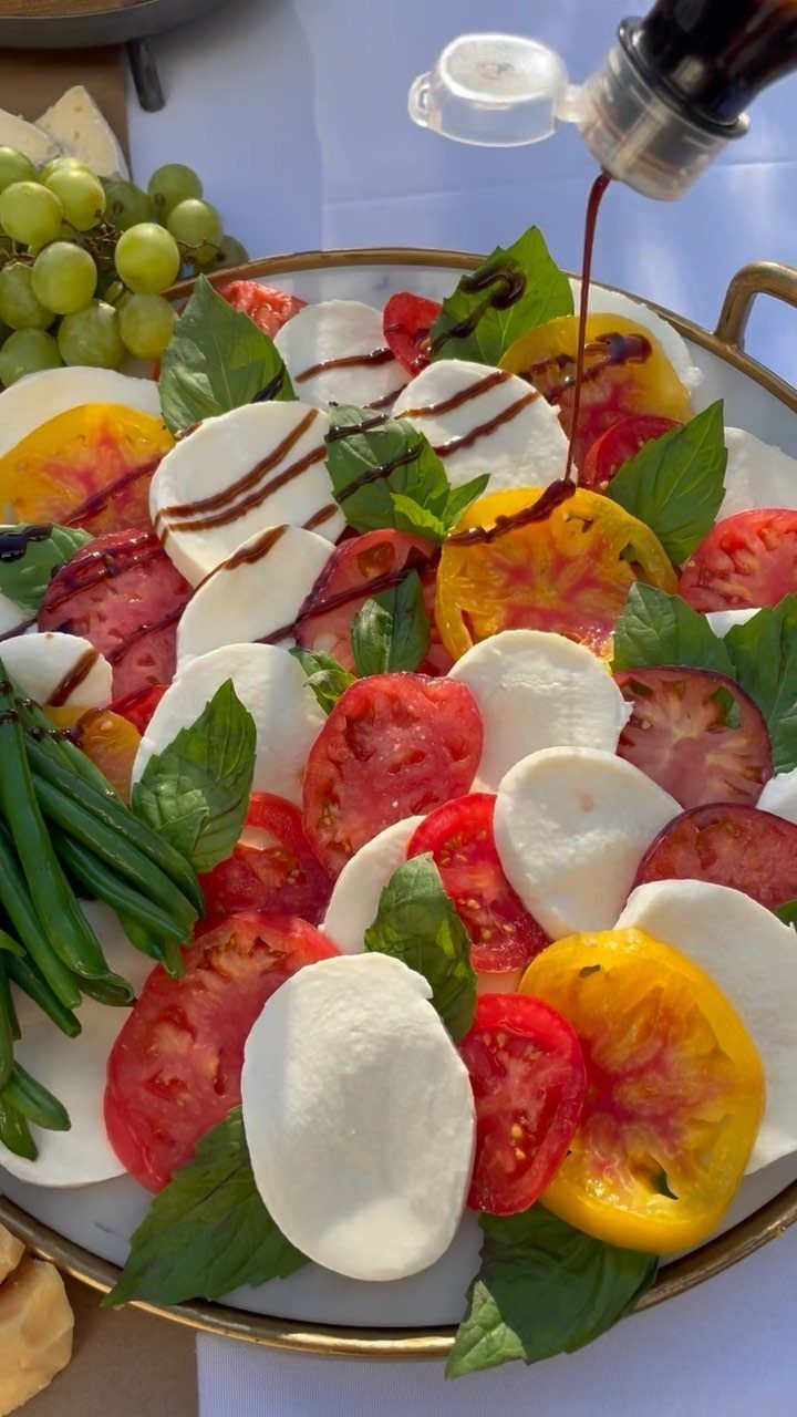 Caprese salad platter with tomatoes and mozzarella being drizzled with balsamic glaze
