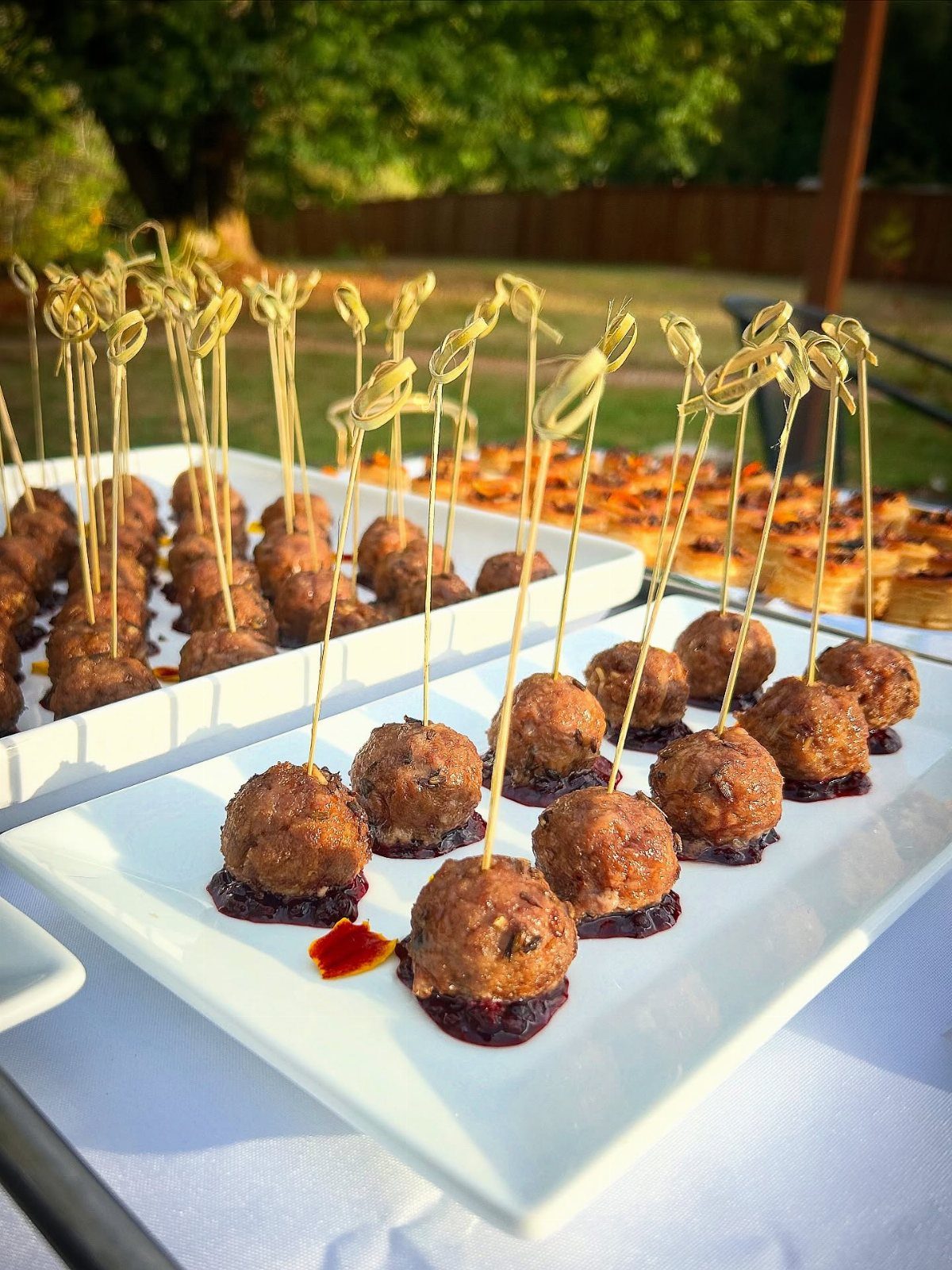 Meatballs with red jam on white platters with decorative bamboo knot skewers
