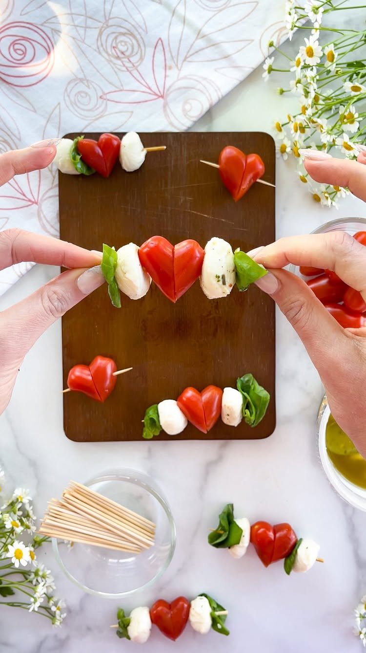 Caprese salad skewers with heart-shaped tomatoes, mozzarella, and basil on a wooden board.