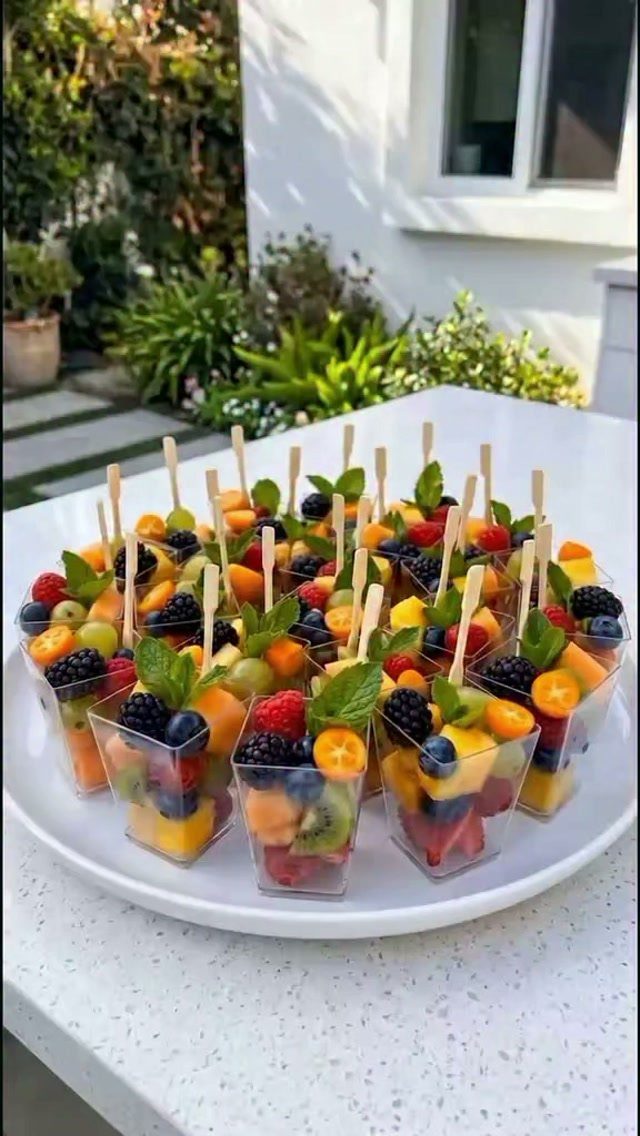 Mixed fruit cups with wooden picks arranged on a white platter outdoors.