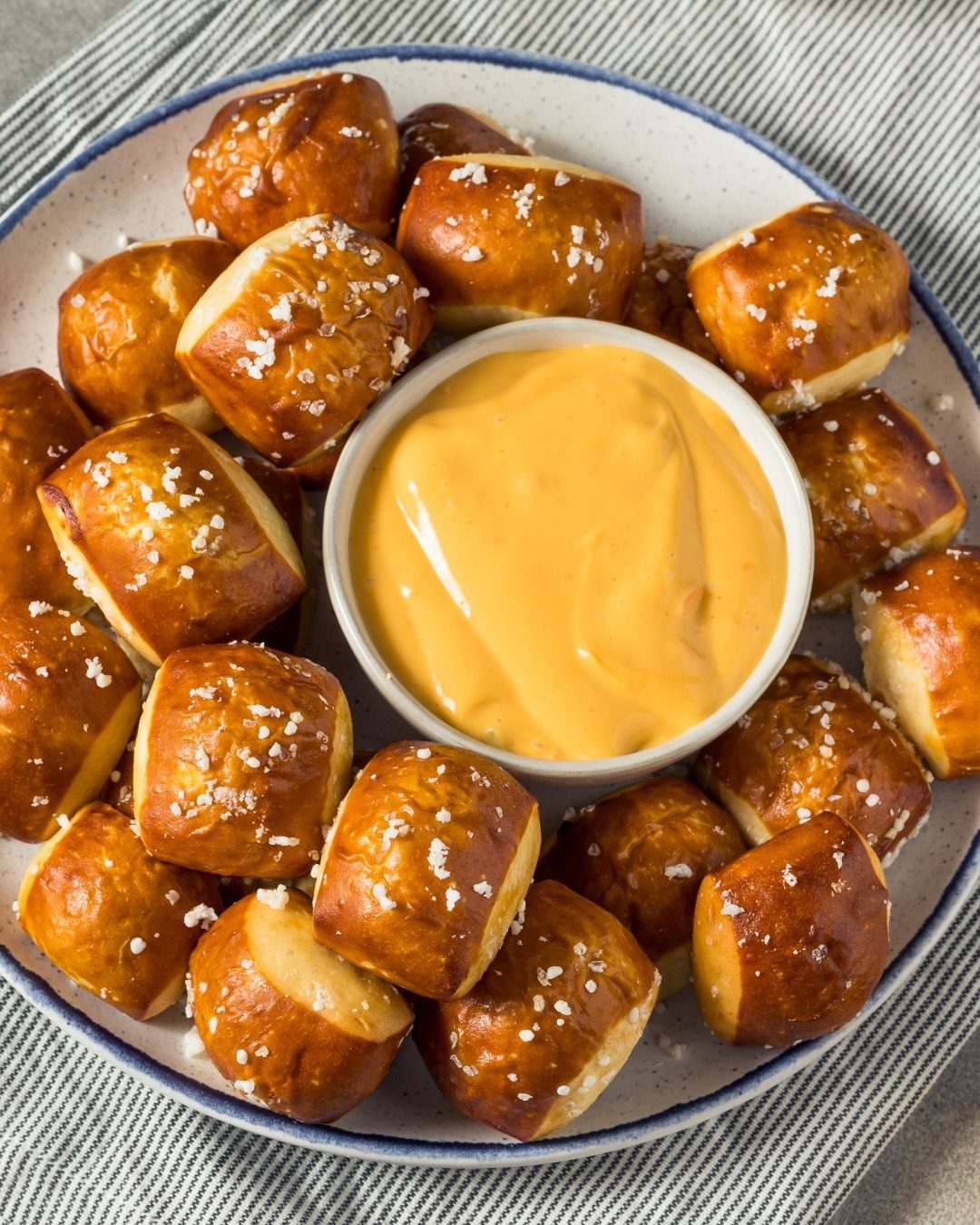 Soft pretzel bites with coarse salt surrounding a bowl of cheese dip.