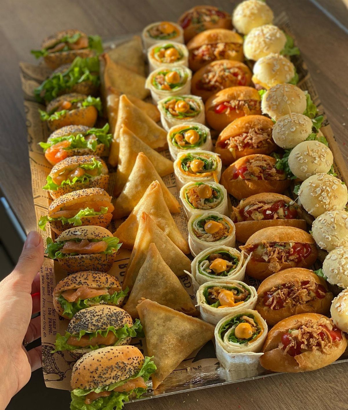 Assorted finger foods including mini burgers, samosas, and wraps on a platter.