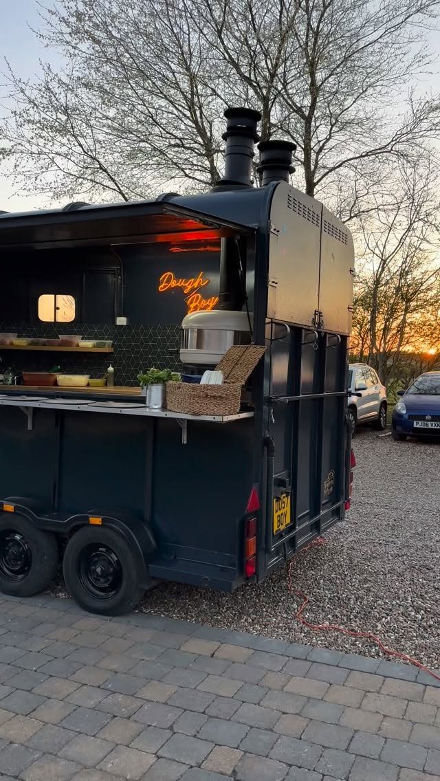 Black mobile food trailer with an open serving window parked outdoors at sunset.