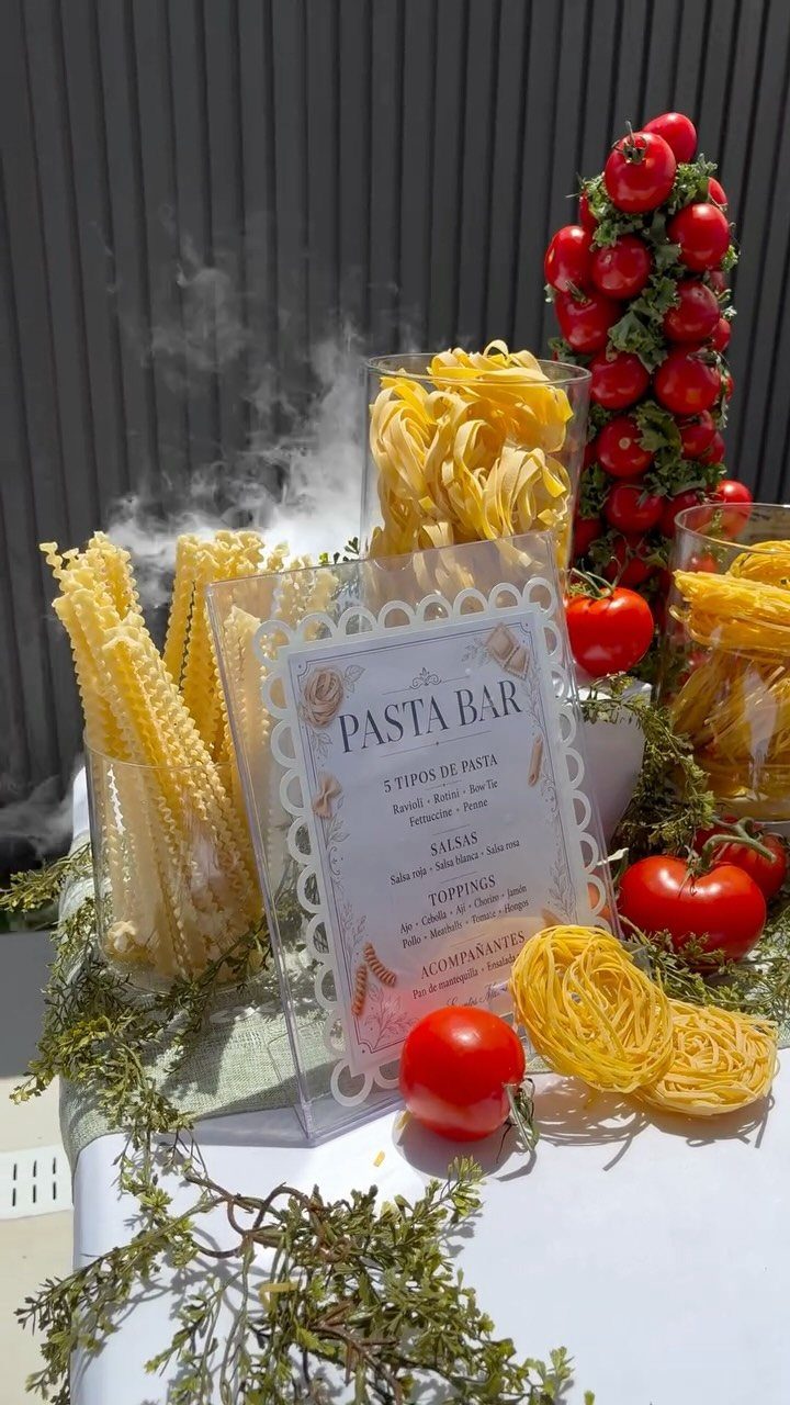 Pasta bar setup with various dry pasta, red tomatoes, and a descriptive sign.