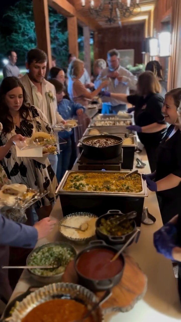 Guests at a wedding buffet serving themselves from a taco bar with toppings.