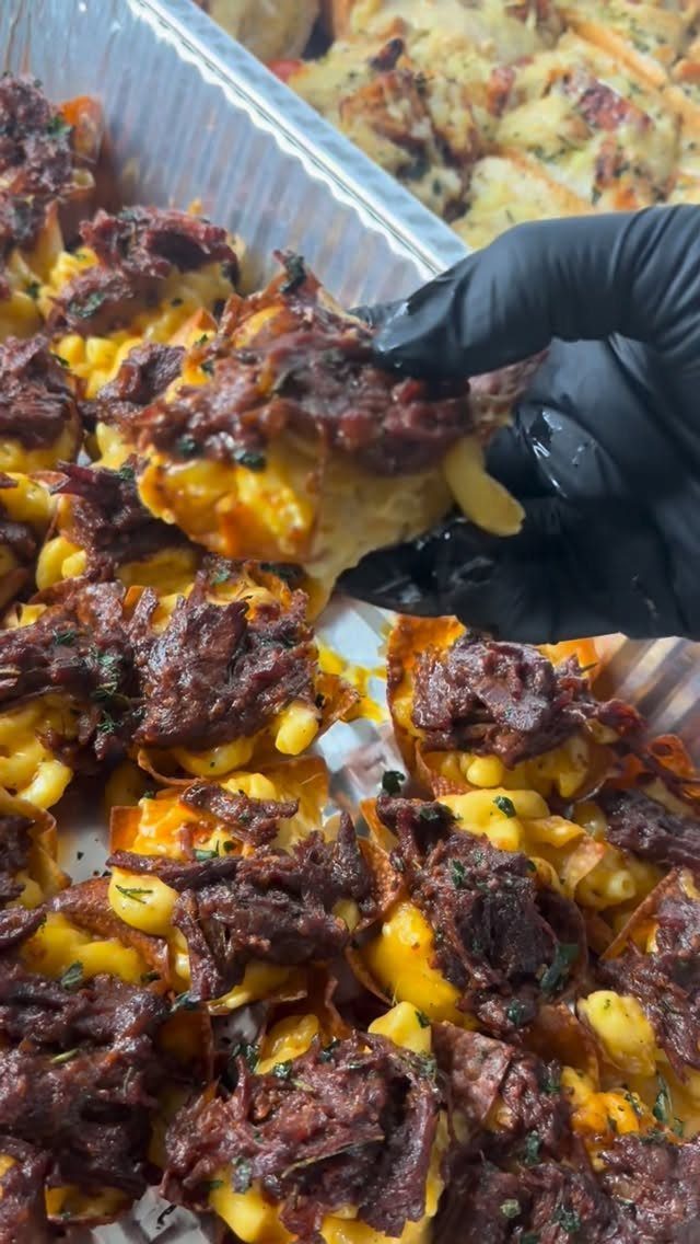 Macaroni and cheese appetizers topped with shredded beef in a foil tray.