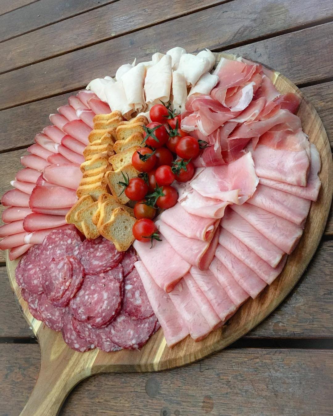 Cold meat platter with salami, ham, prosciutto, cheese, and tomatoes on wooden board.