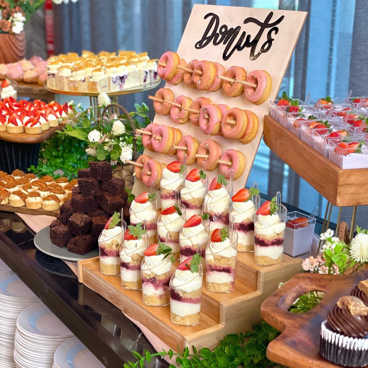 Dessert bar with a donut wall, strawberry parfaits, brownies, and mini tarts.