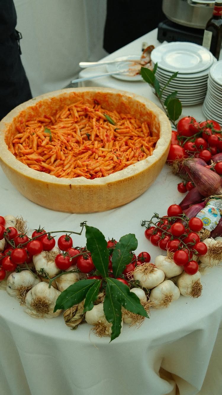 Pasta with red sauce served in a cheese wheel surrounded by fresh vegetables