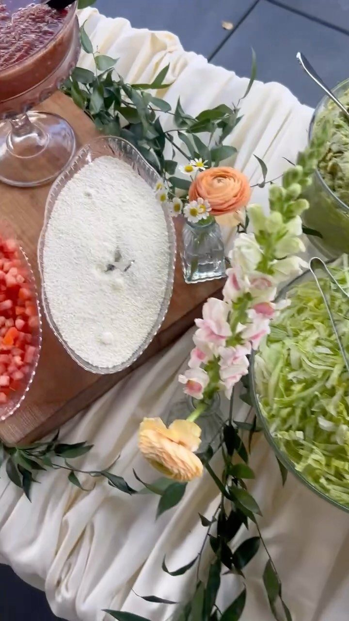 Buffet table with fresh salads, fruit, and floral decorations on white draped fabric.