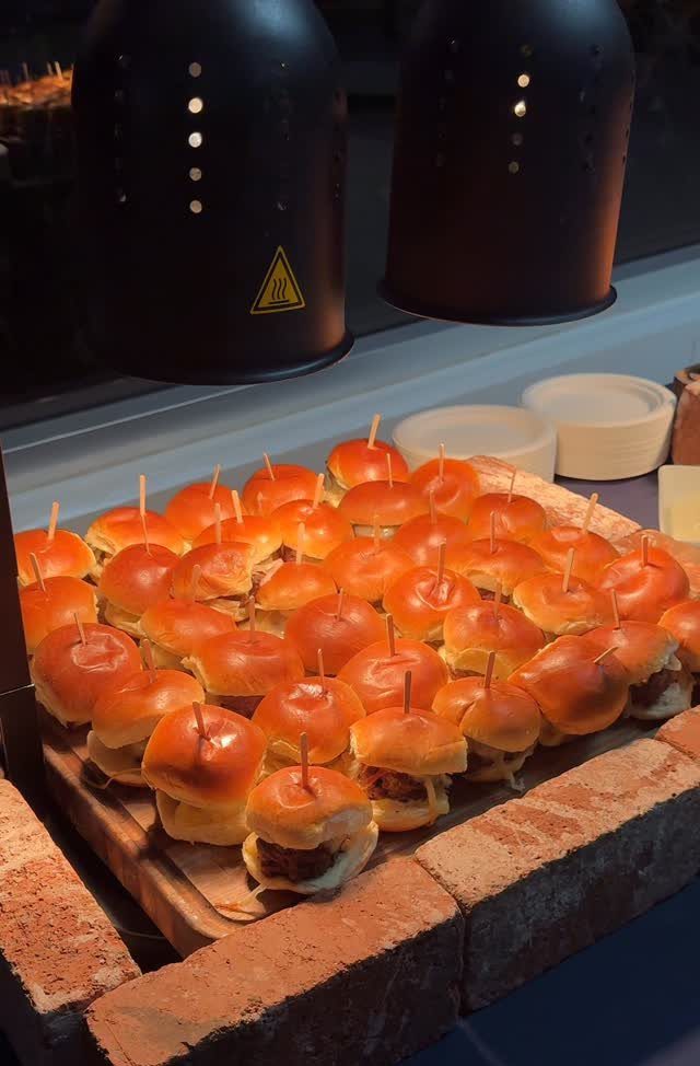 Mini sliders with toothpicks arranged on a wooden board atop a brick ledge.