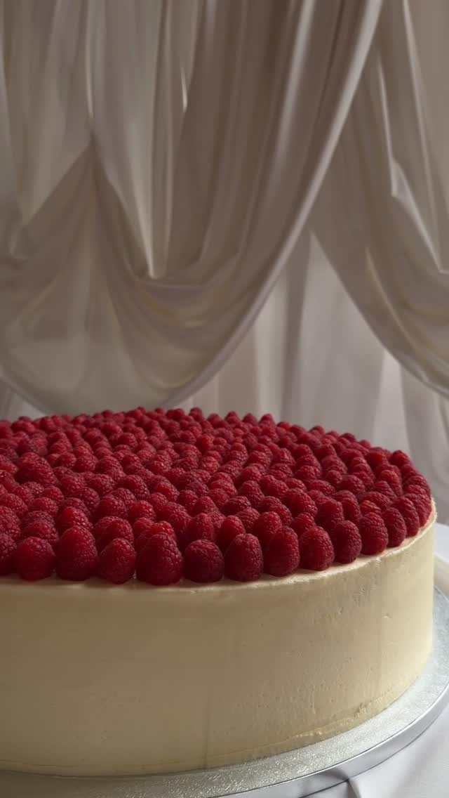 White cheesecake topped with fresh red raspberries against draped white fabric background