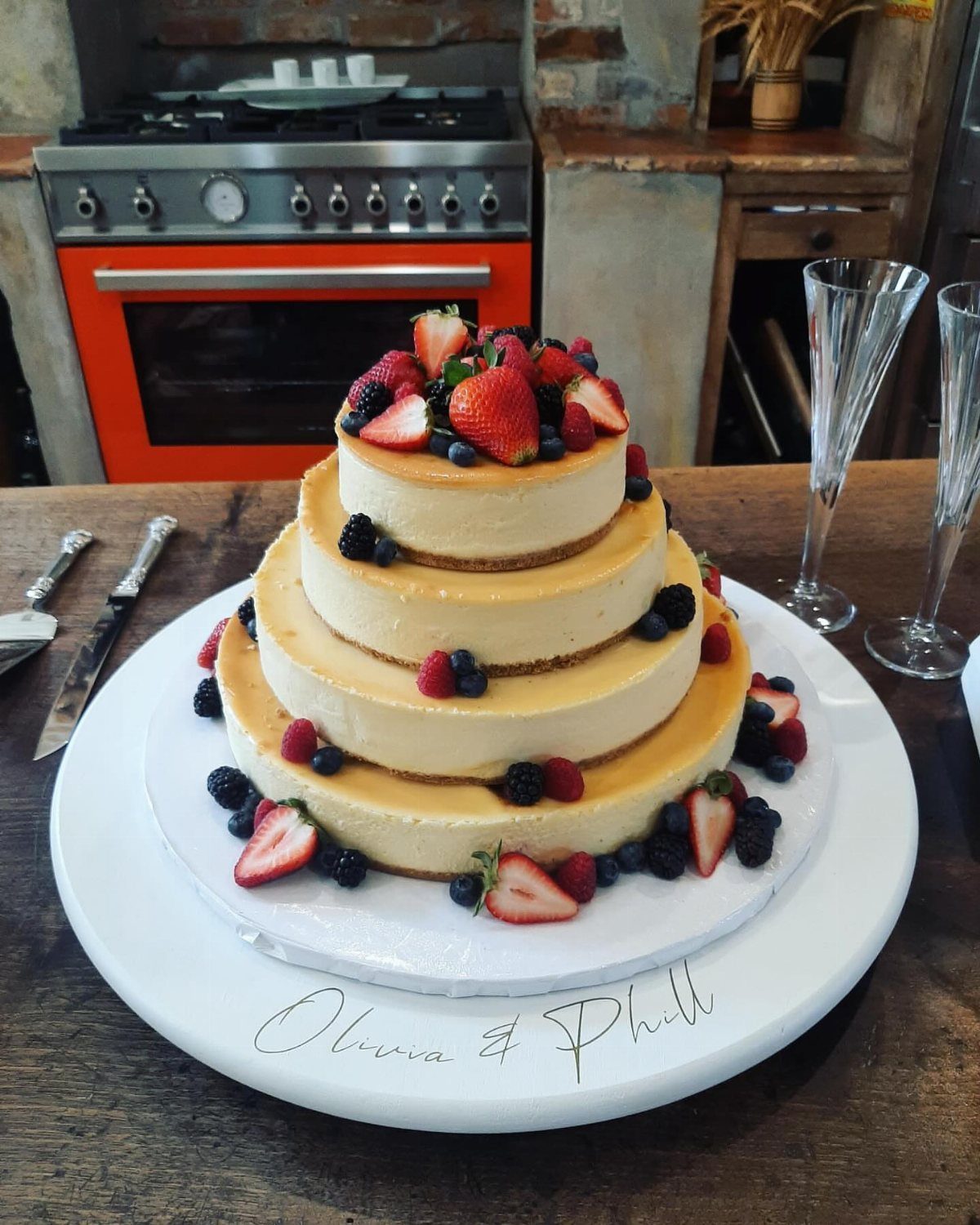 Three-tiered cheesecake decorated with fresh berries on a white platter in a kitchen