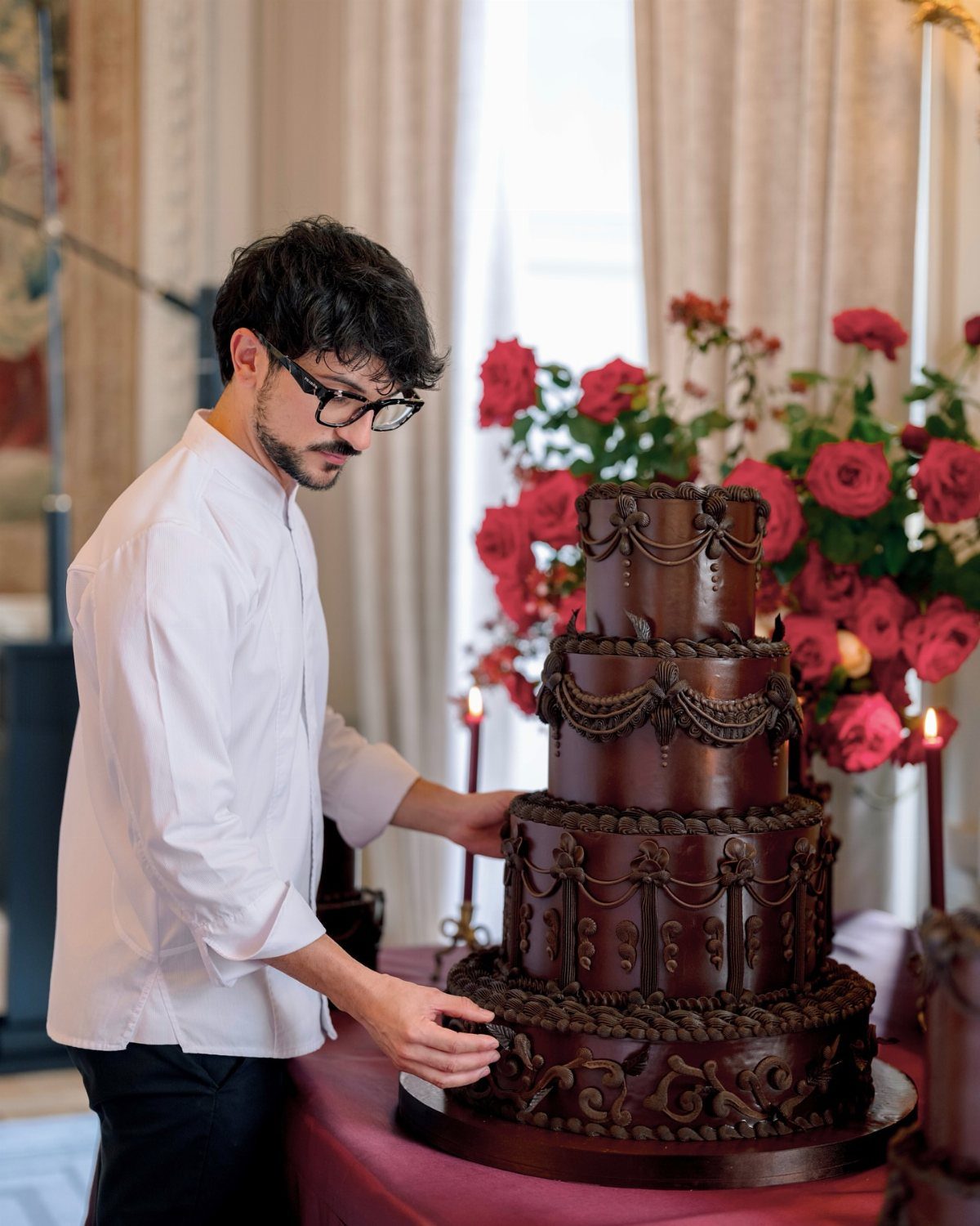 Four-tiered dark chocolate wedding cake with intricate swirls and a pastry chef.