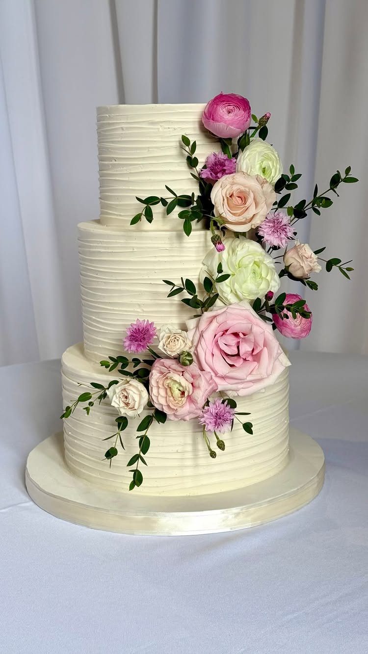 Three-tiered white cake with a cascade of pink and white flowers and greenery.