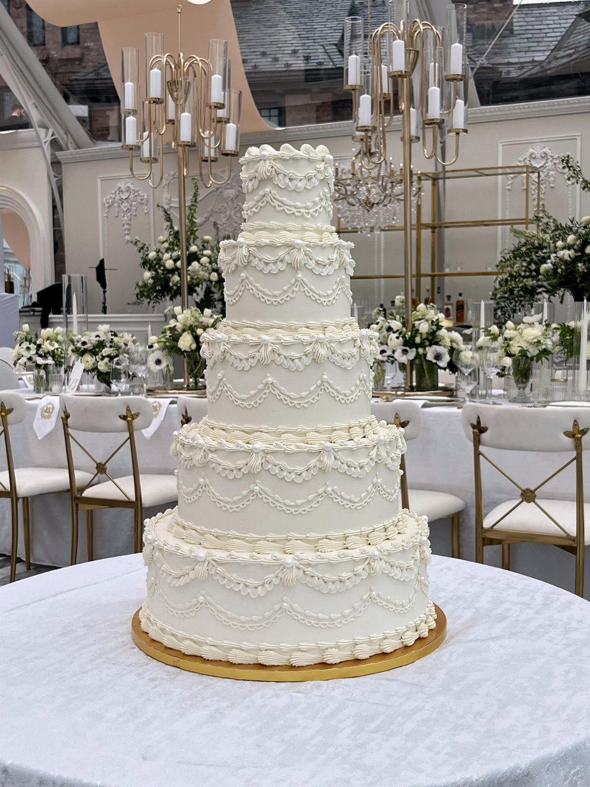 Five-tier white wedding cake with piped frosting swags on a marble table.