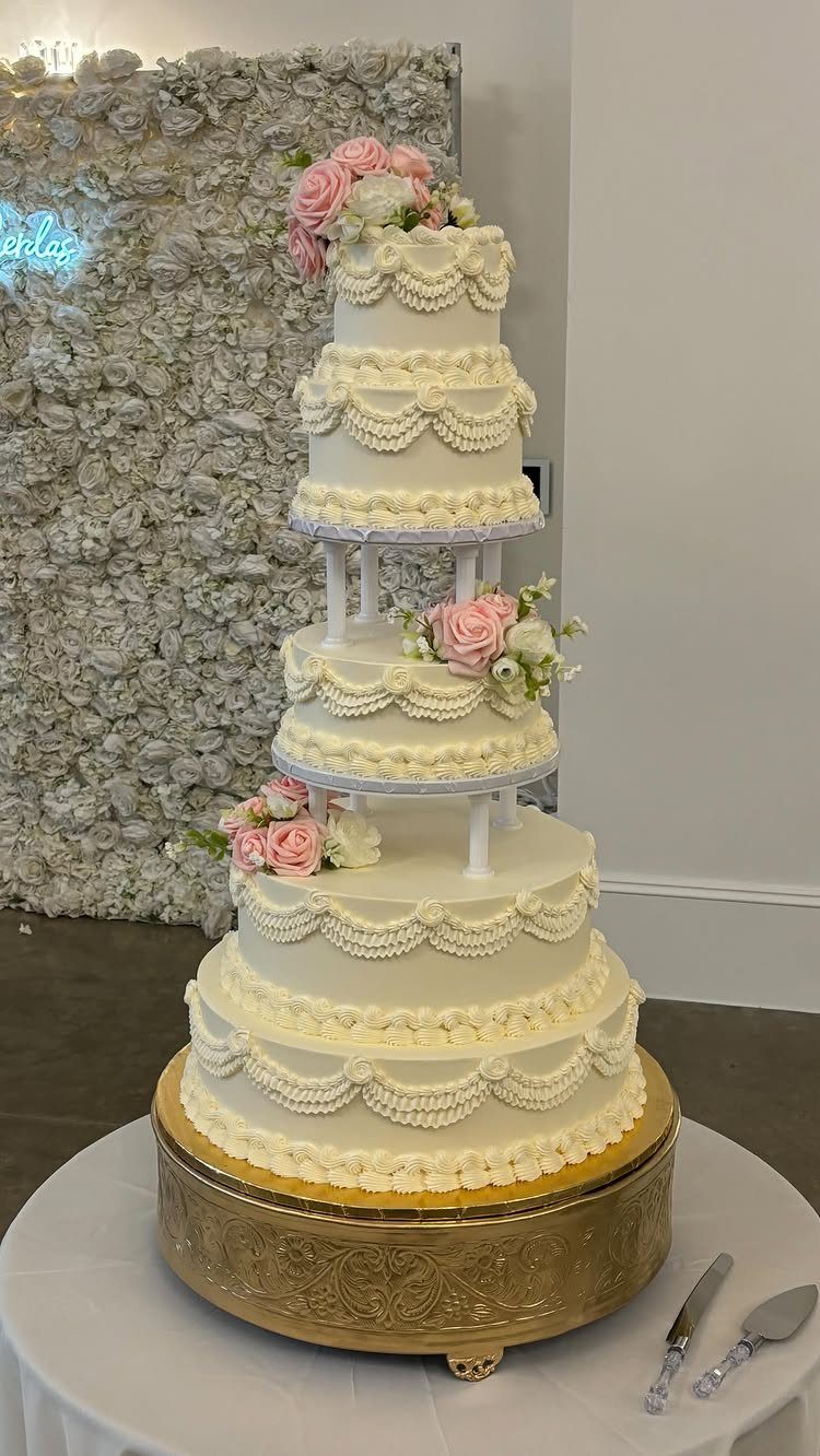 Multi-tiered white wedding cake with lace-like frosting and pink roses on gold stand