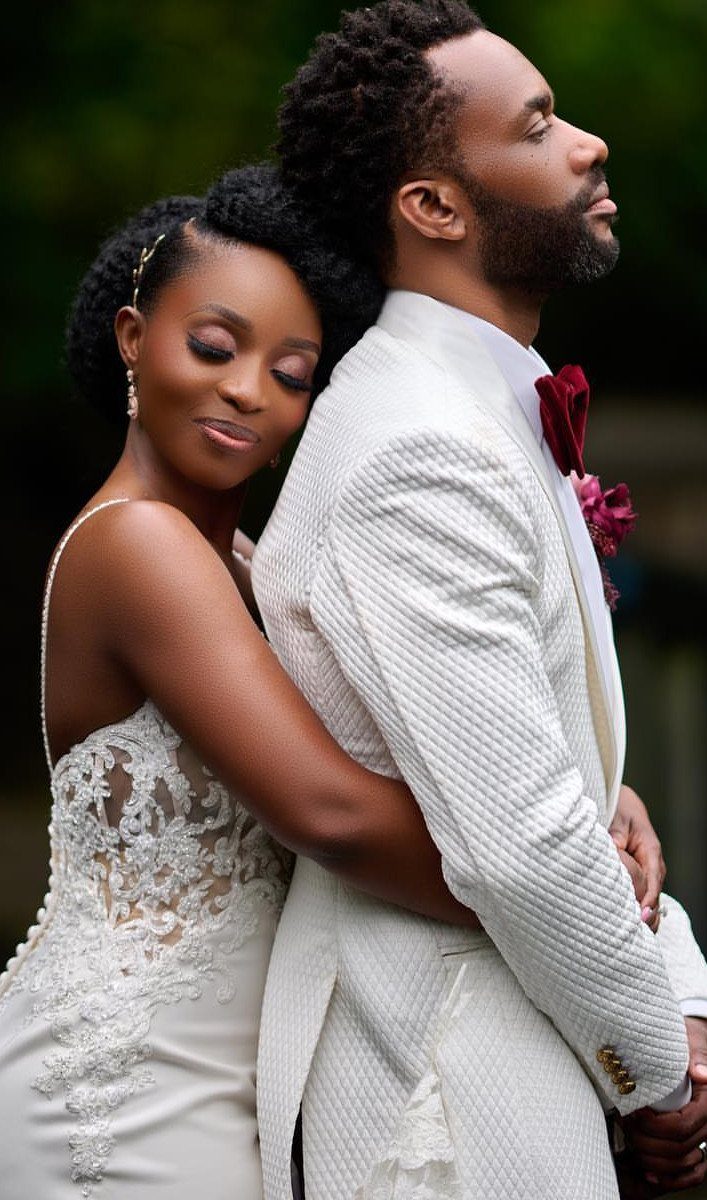 Bride leaning her head against the groom's back in white wedding attire outdoors.
