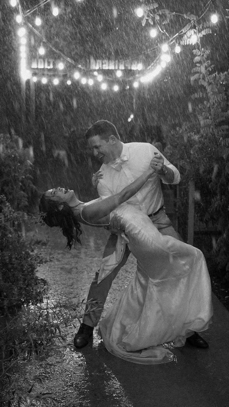 Groom dipping bride in a white wedding dress during a rainy night outdoors.