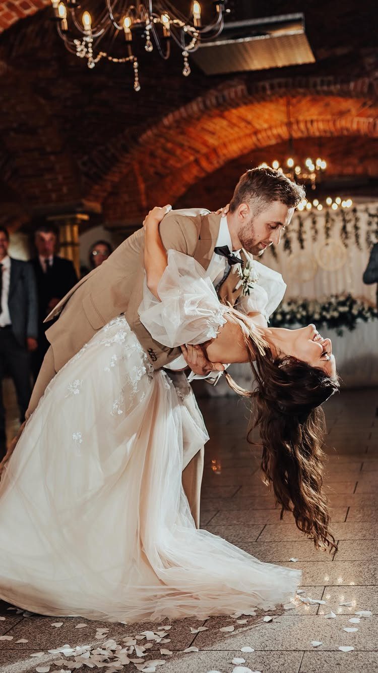 Groom dipping bride in white dress during their first dance in arched hall