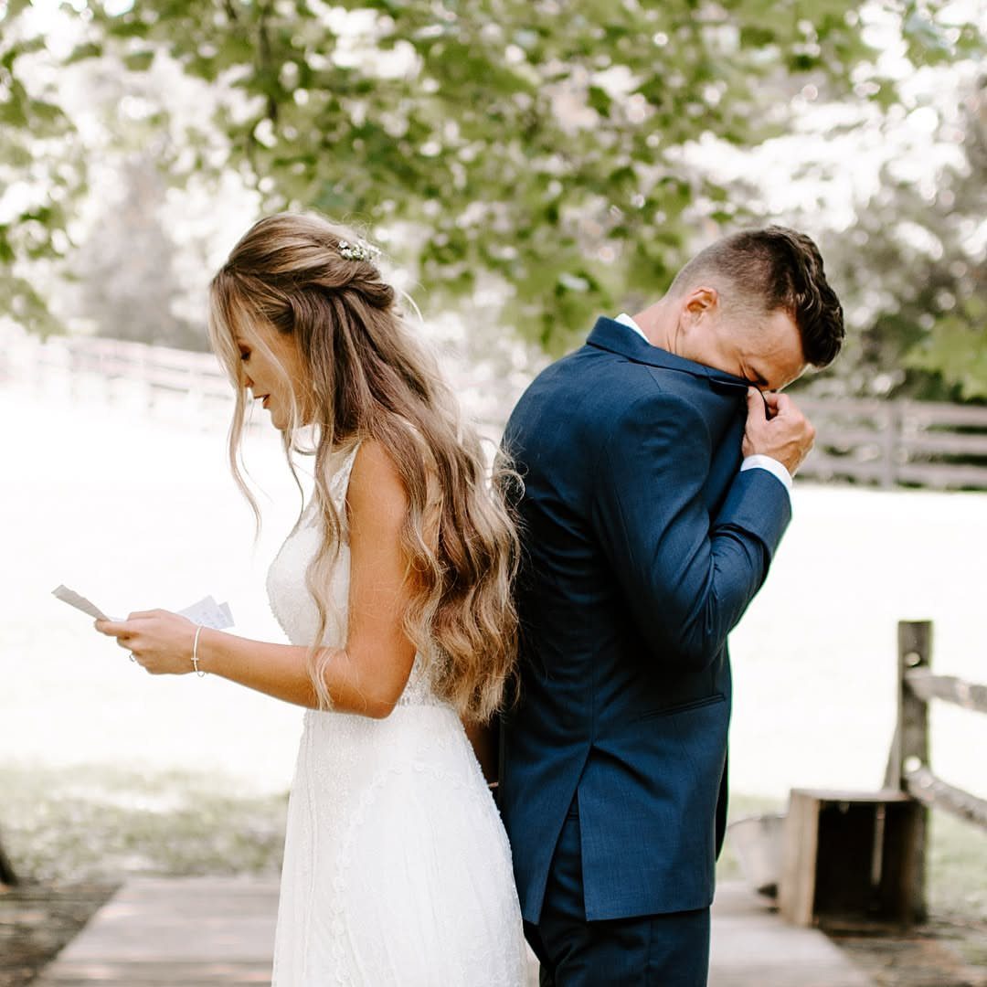 Bride reading a letter while groom cries standing back-to-back in outdoor wedding setting