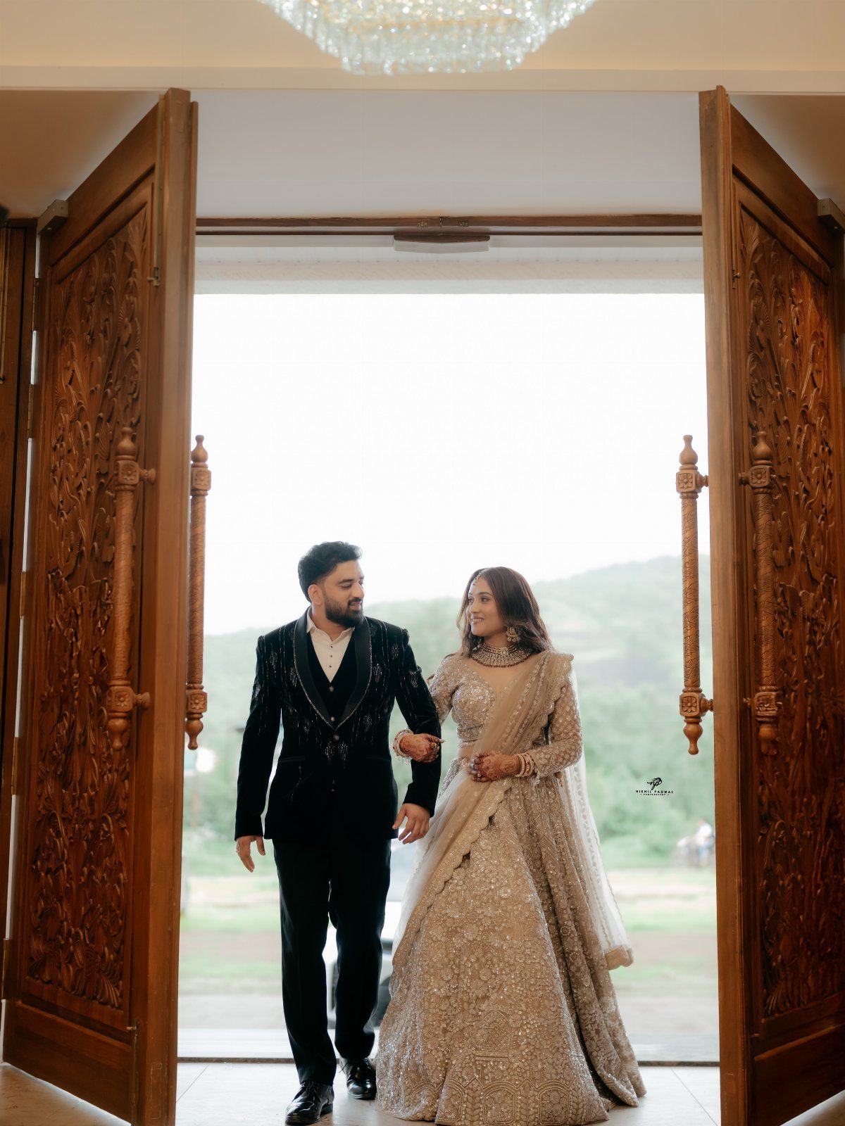 Couple in formal wedding attire standing together framed by large carved wooden doors.