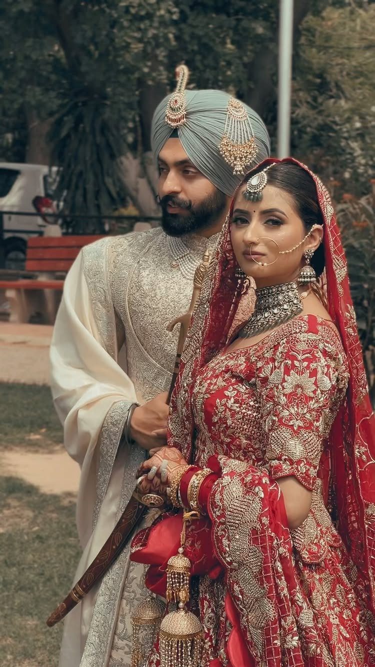 Indian wedding couple in regal traditional attire posing outdoors in red and cream.