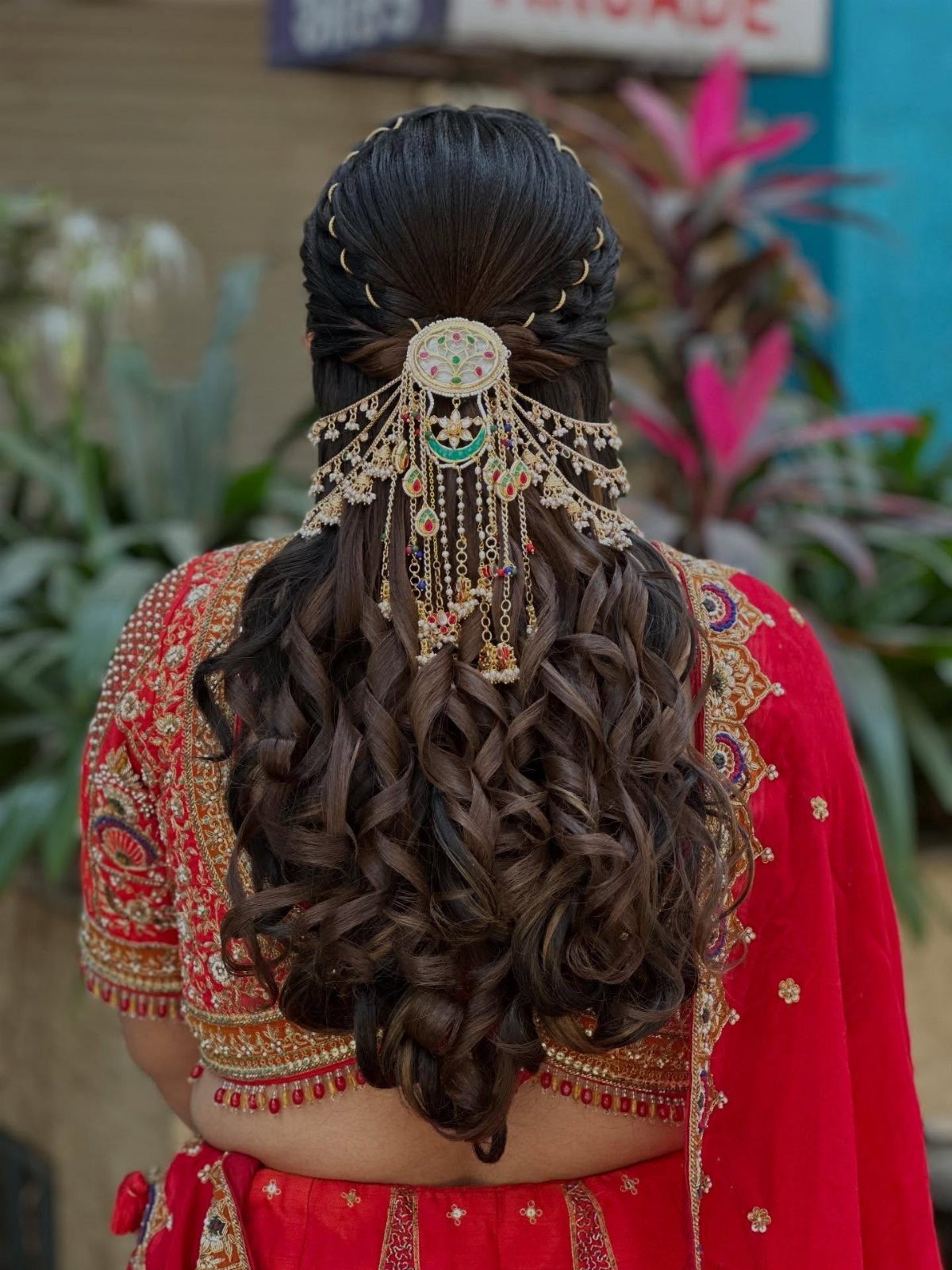 Dark curly bridal hair with a large gold dangling hair accessory and red attire