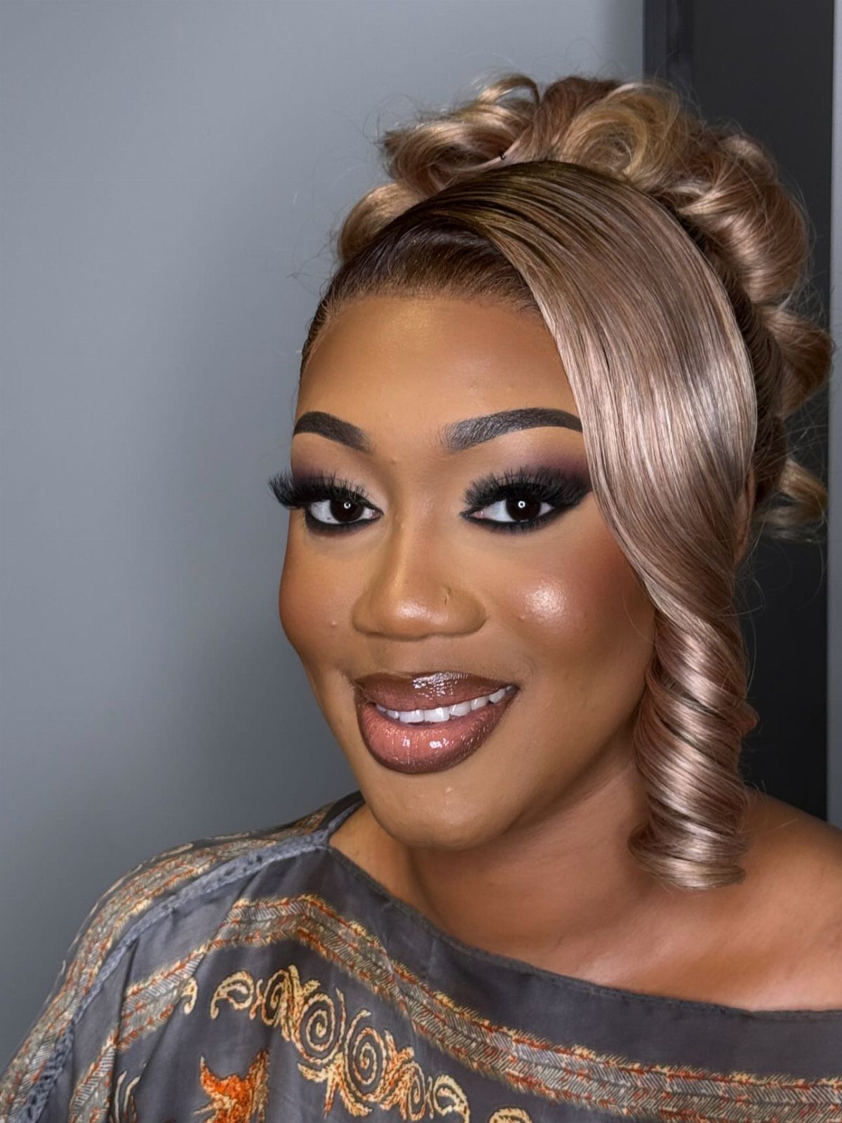 Woman with a voluminous blonde bridal updo and a large face-framing curl.