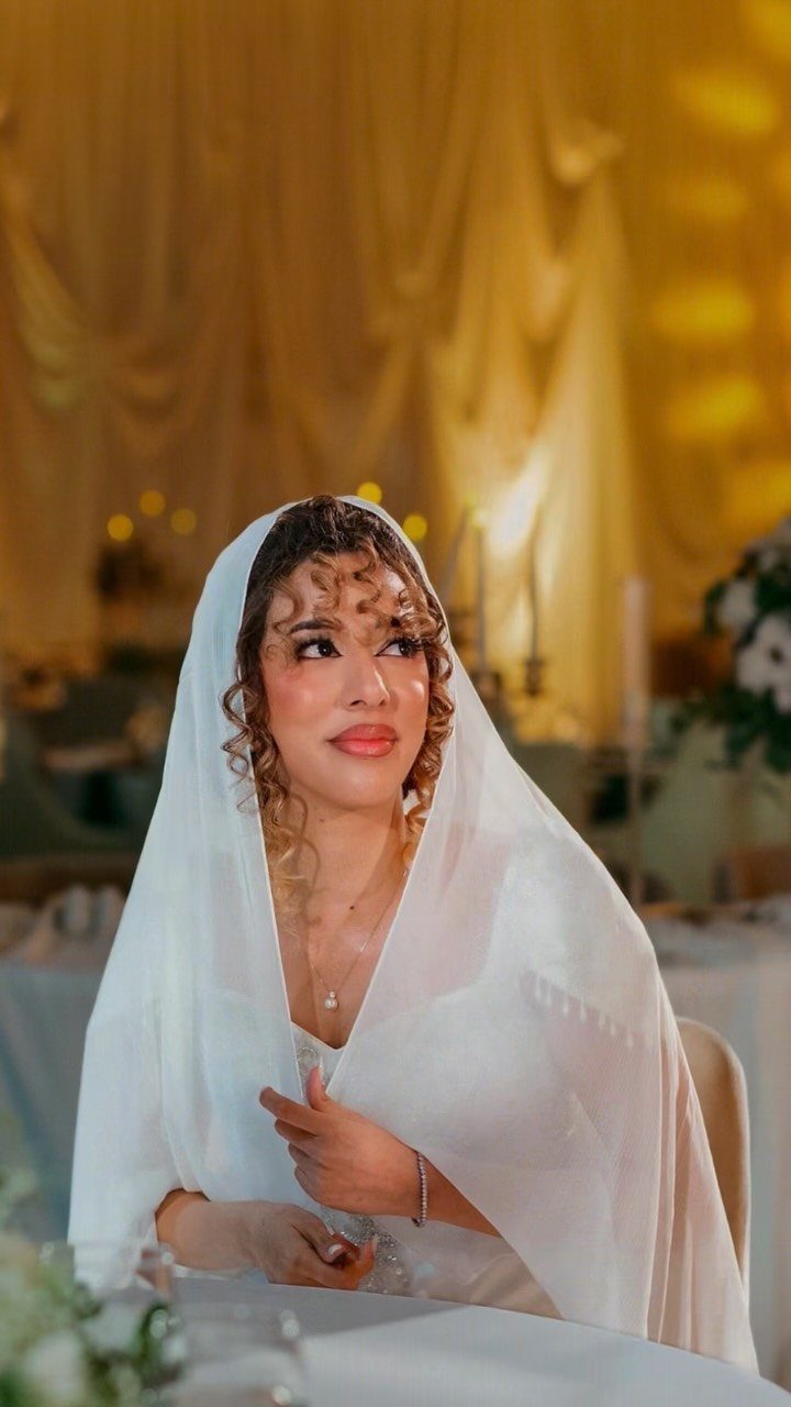 Bride with loose brown curls wearing a white veil and wedding dress.