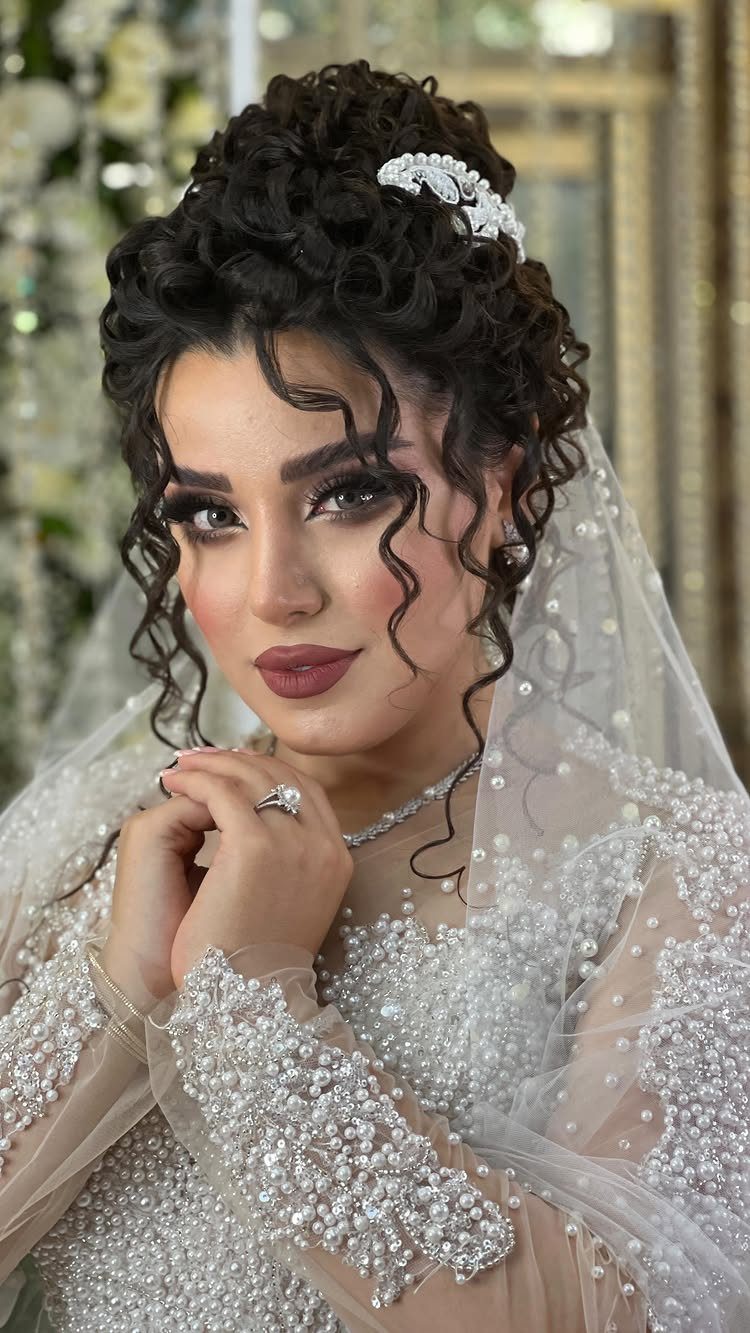 Woman with curly bridal updo, white hair accessory, and pearl-embellished wedding dress.