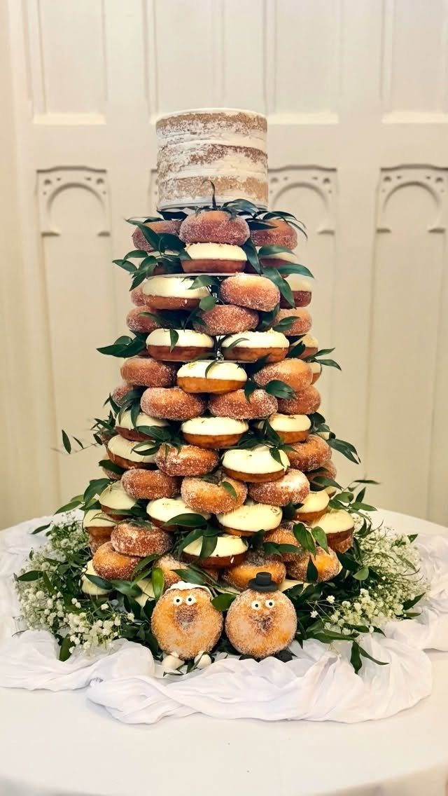 Doughnut tower stacked with powdered and glazed doughnuts and topped with a cake.
